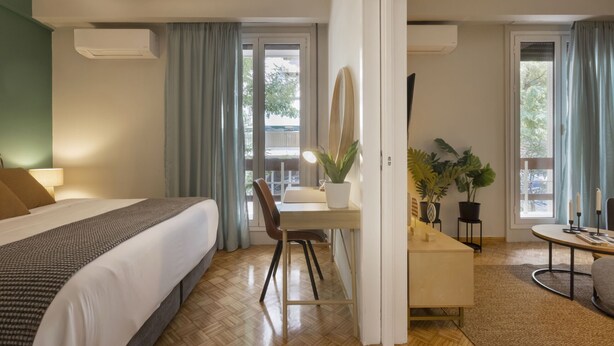 A hotel room with a bed, a desk, a chair, a small table, and a potted plant. - Pausaniou 8 studio-Eclectic Studio near Kal (Athens)