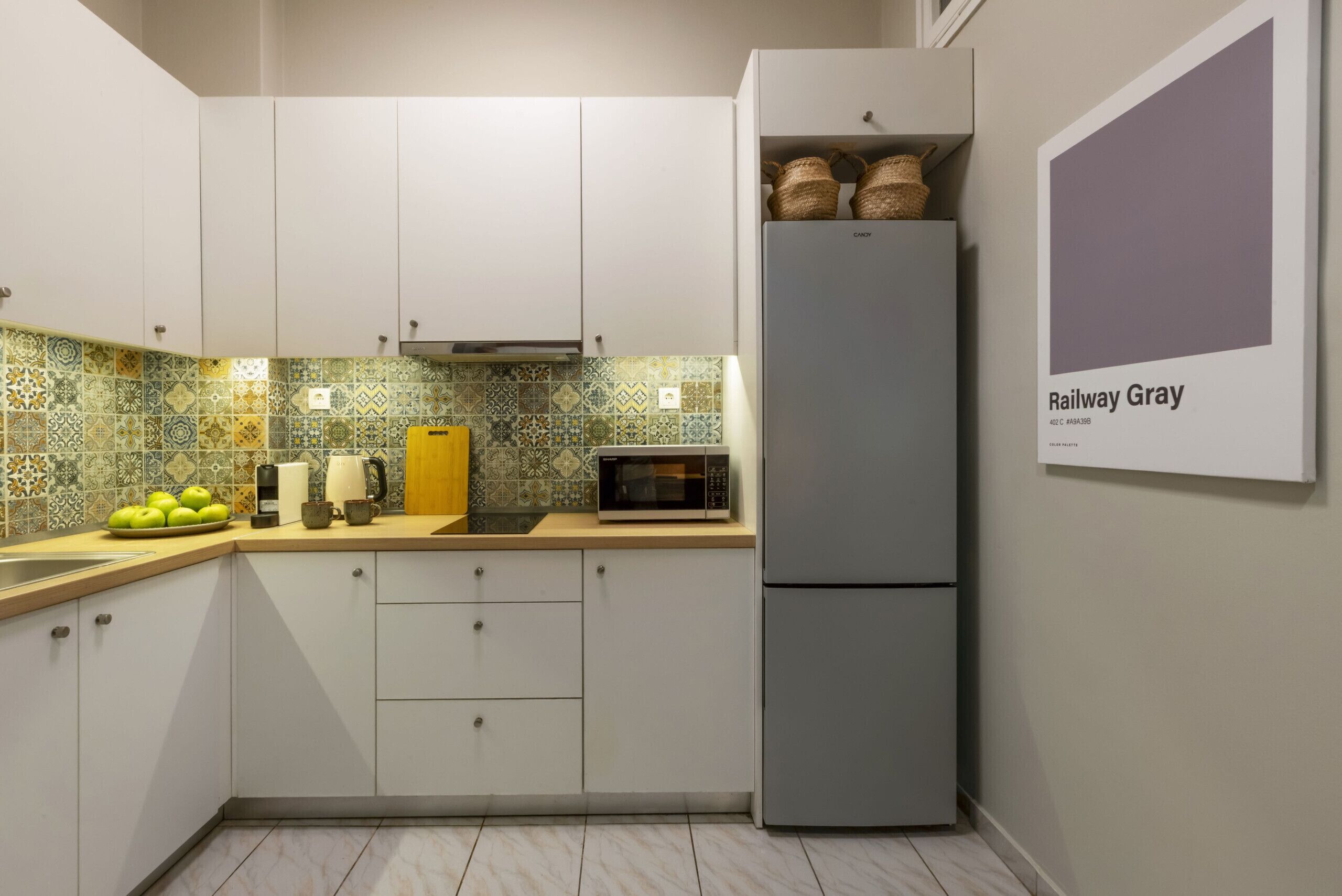 A kitchen with white cabinets, a grey refrigerator, a microwave, and a tiled backsplash.