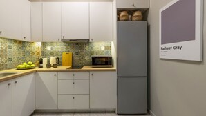 A compact kitchen with white cabinets, a grey refrigerator, a microwave, and a tiled backsplash. - Pausaniou 8 studio-Eclectic Studio near Kal (Athens)