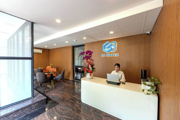 A reception area with a receptionist at a desk, a logo on the wall, and a seating area with chairs and a table. - G8 Le Van Sy Hotel Saigon (Ho Chi Minh City)