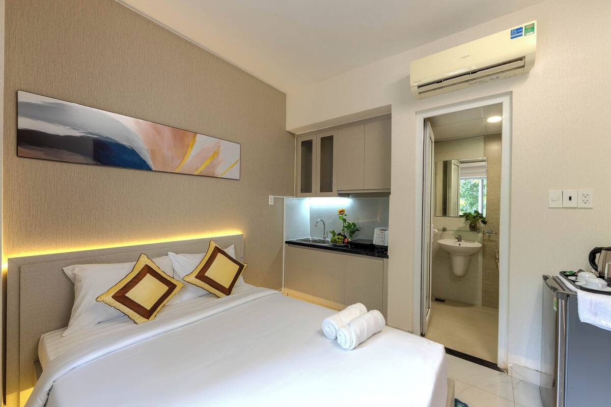 A hotel room with a bed, a painting, a kitchenette, and a bathroom.