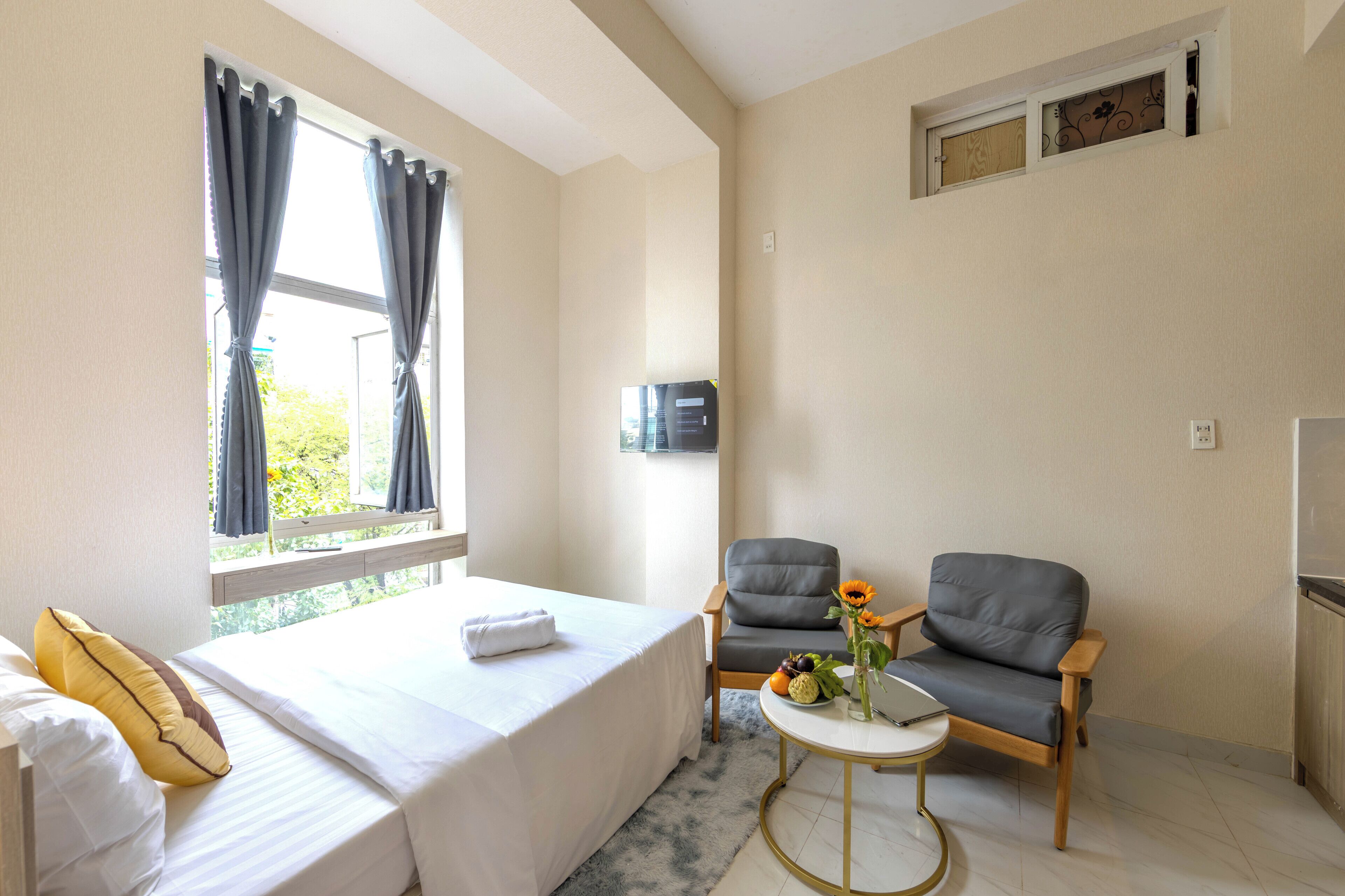 A hotel room with a bed, two chairs, a small table with a vase of flowers, and a TV on the wall.