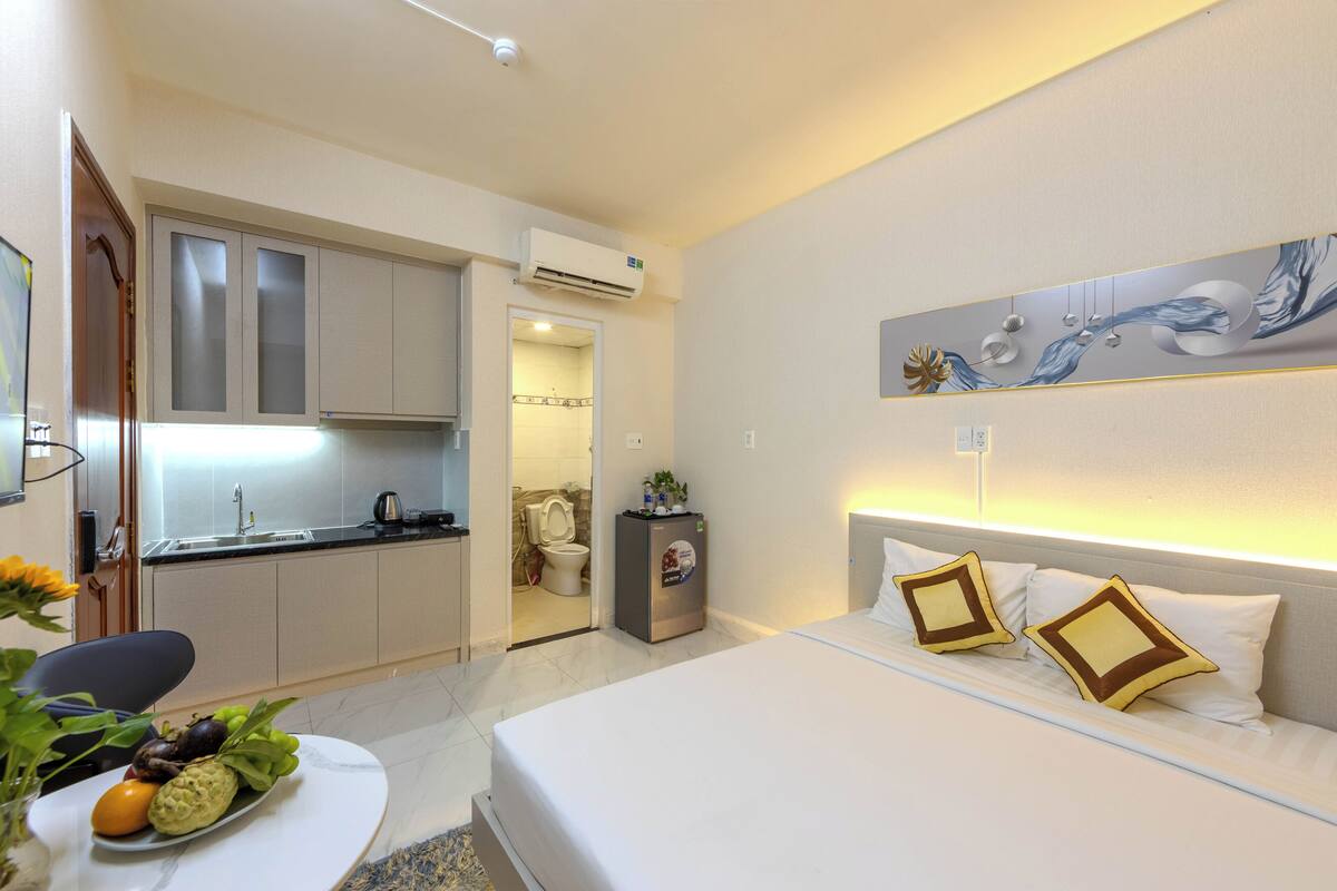 A hotel room with a bed, bedside table, and a view into the kitchen.