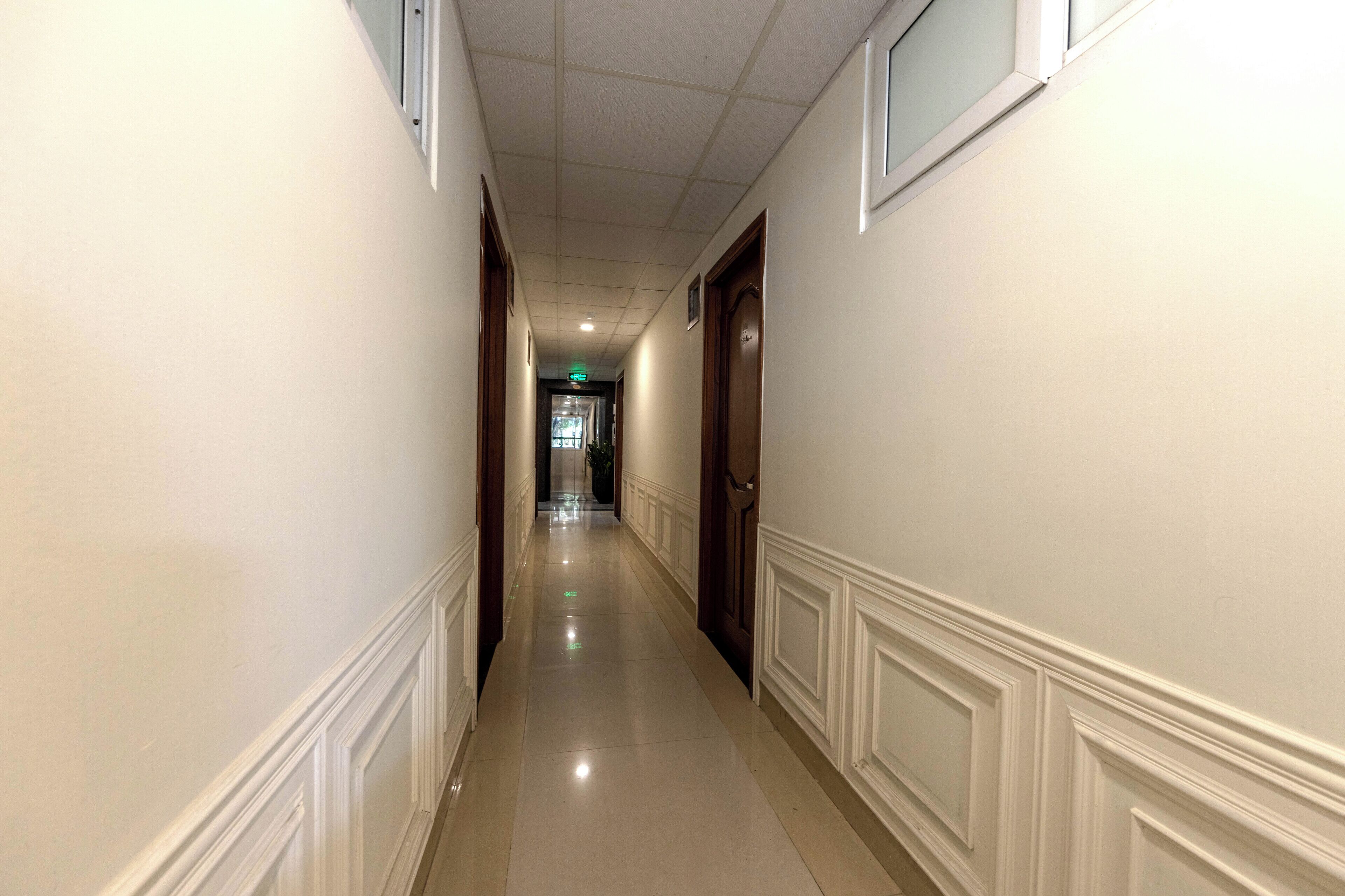 Un long couloir étroit aux murs blancs et aux portes en bois.