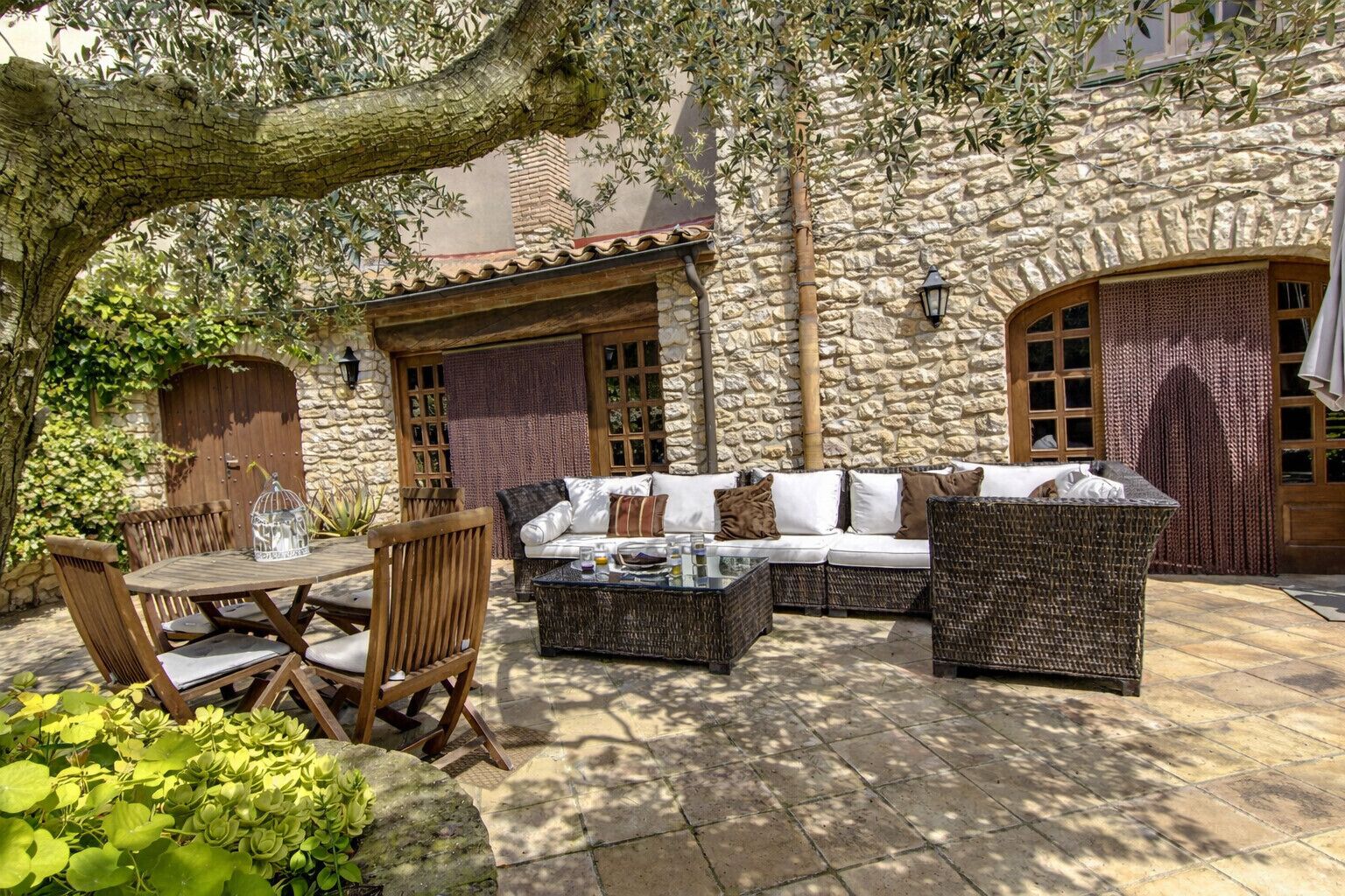 Un edificio de piedra con un patio amueblado, una mesa y una jaula decorativa para pájaros.