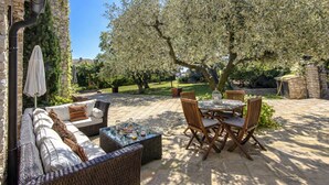 Un espacio de patio al aire libre con un sofá, una mesa de comedor y sillas, rodeado de árboles y un muro de piedra.