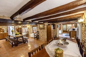 A rustic interior with exposed wooden beams, stone walls, a dining area with wooden furniture, and a kitchen visible through an open doorway. - Majestic history for 32 guests, 10km to the beach (Santa Oliva)