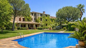 Una piscina con solárium de piedra, rodeada por un césped cuidado y árboles.