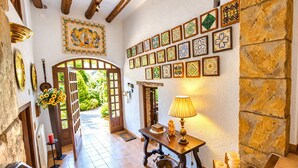 Un pasillo con una puerta de madera que da a un jardín, una pared adornada con azulejos y una mesa con una lámpara y un cuenco.