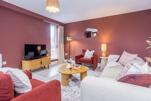 Ein modernes Wohnzimmer mit Flachbildfernseher, roten und weißen Sofas, einem Holztisch und einem großen Spiegel.