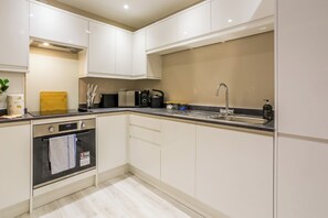A modern kitchen with white cabinets, a black countertop, a built-in oven, a microwave, a kettle, and a sink. - Toast Stays - The Ruby at Parsons House (Washington)