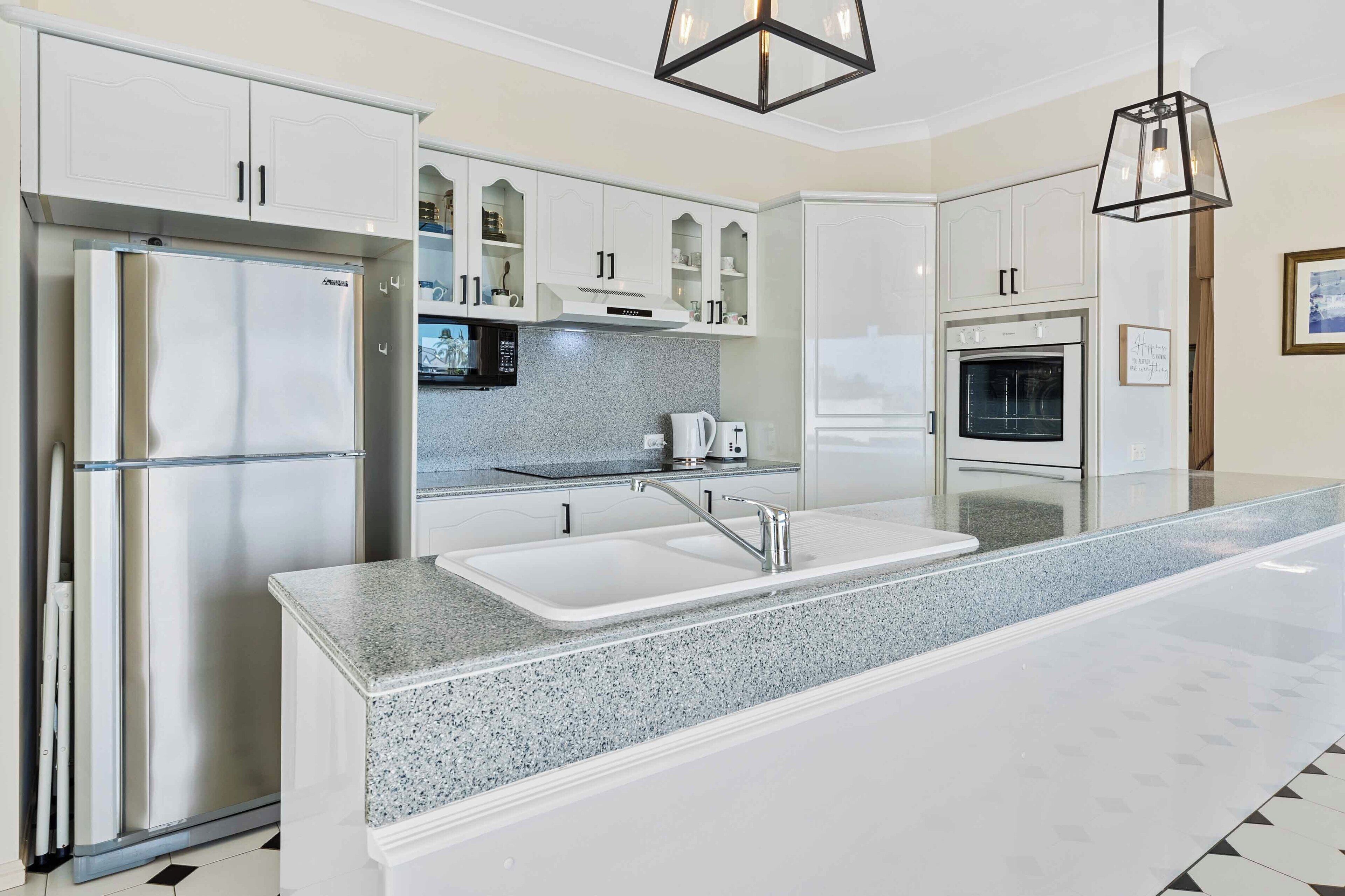 A modern kitchen with white cabinetry, a stainless steel refrigerator, a double sink, and a built-in oven.