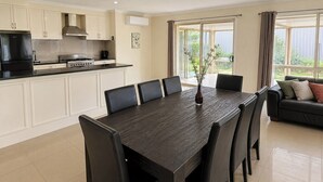 A modern kitchen with white cabinets, a black countertop, and a dining area with a dark wooden table and chairs. - Relaxed Mount Gambier home with backyard (Mount Gambier)