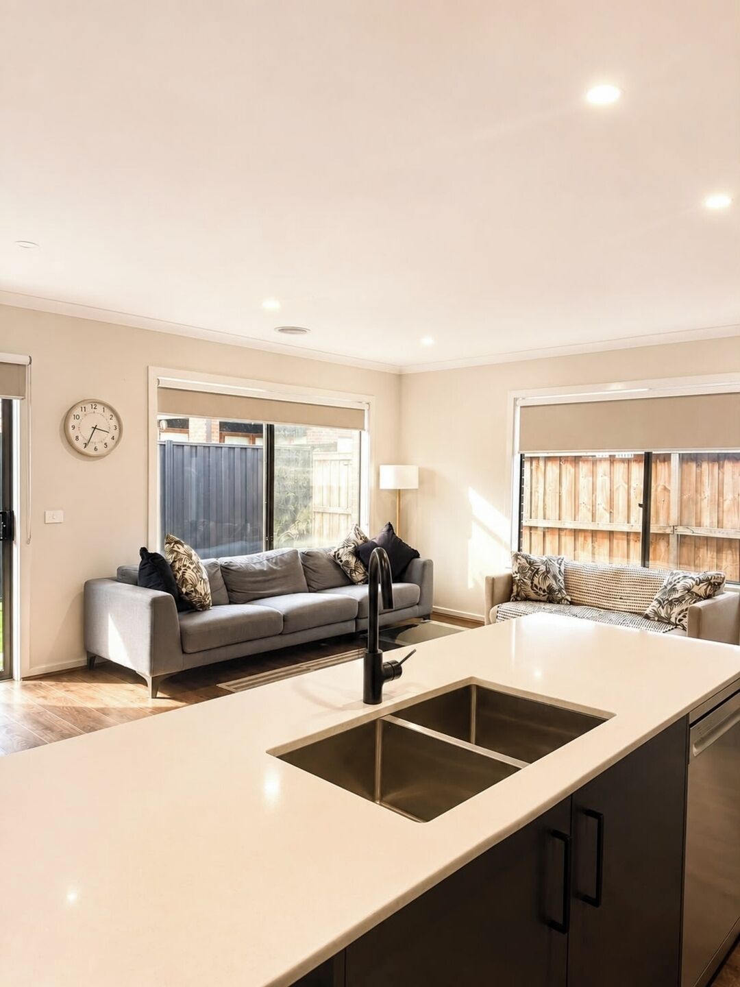 A modern kitchen with a central island, a grey sofa, and a clock on the wall.