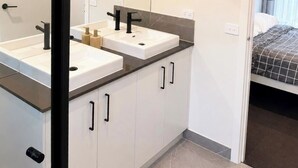 Et moderne badeværelse med to håndvaske, et stort spejl og et walk-in closet.