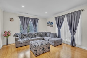 A modern living room with a grey sectional sofa, a patterned ottoman, and grey curtains.