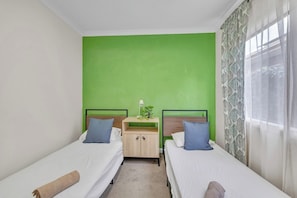 A room with two beds, a bedside table with a lamp, and a green accent wall.
