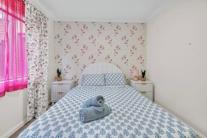 A bedroom with a bed, two bedside tables, a window with curtains, and a patterned wallpaper.
