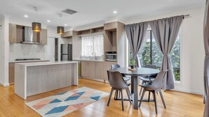 Una cocina moderna con una isla central, mesa de comedor con sillas y vistas a zonas verdes.