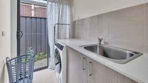 Una cocina con un lavamanos de acero inoxidable, una lavadora y una pequeña ventana con cortina.