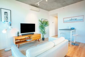 A modern living room with a flat-screen TV, a wooden entertainment unit, a white sofa, a dining area with a small table and chairs, and a potted plant. - Stylish Richmond Pad Walk to Everything (Richmond)