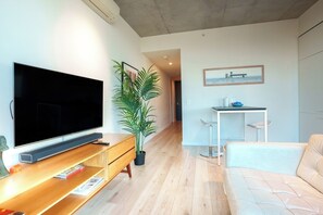 A modern living room with a flat-screen TV, wooden entertainment unit, potted plant, and a dining area with a small table and bar stool. - Stylish Richmond Pad Walk to Everything (Richmond)
