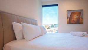 Quarto de hotel com uma cama grande, janela vista para a cidade e um quadro na parede.