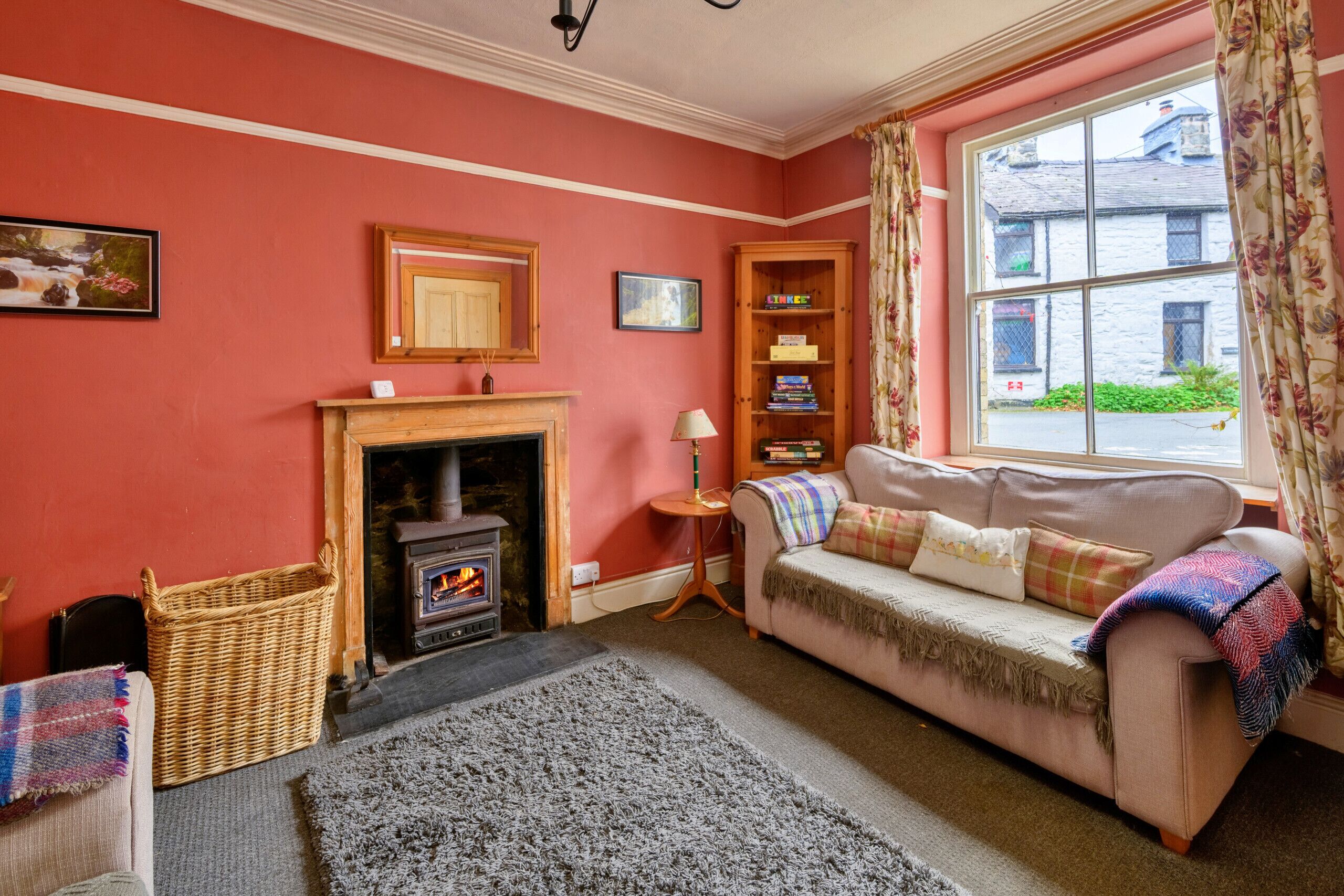 A cozy living room with a fireplace, a sofa, a bookshelf, and a window with curtains.