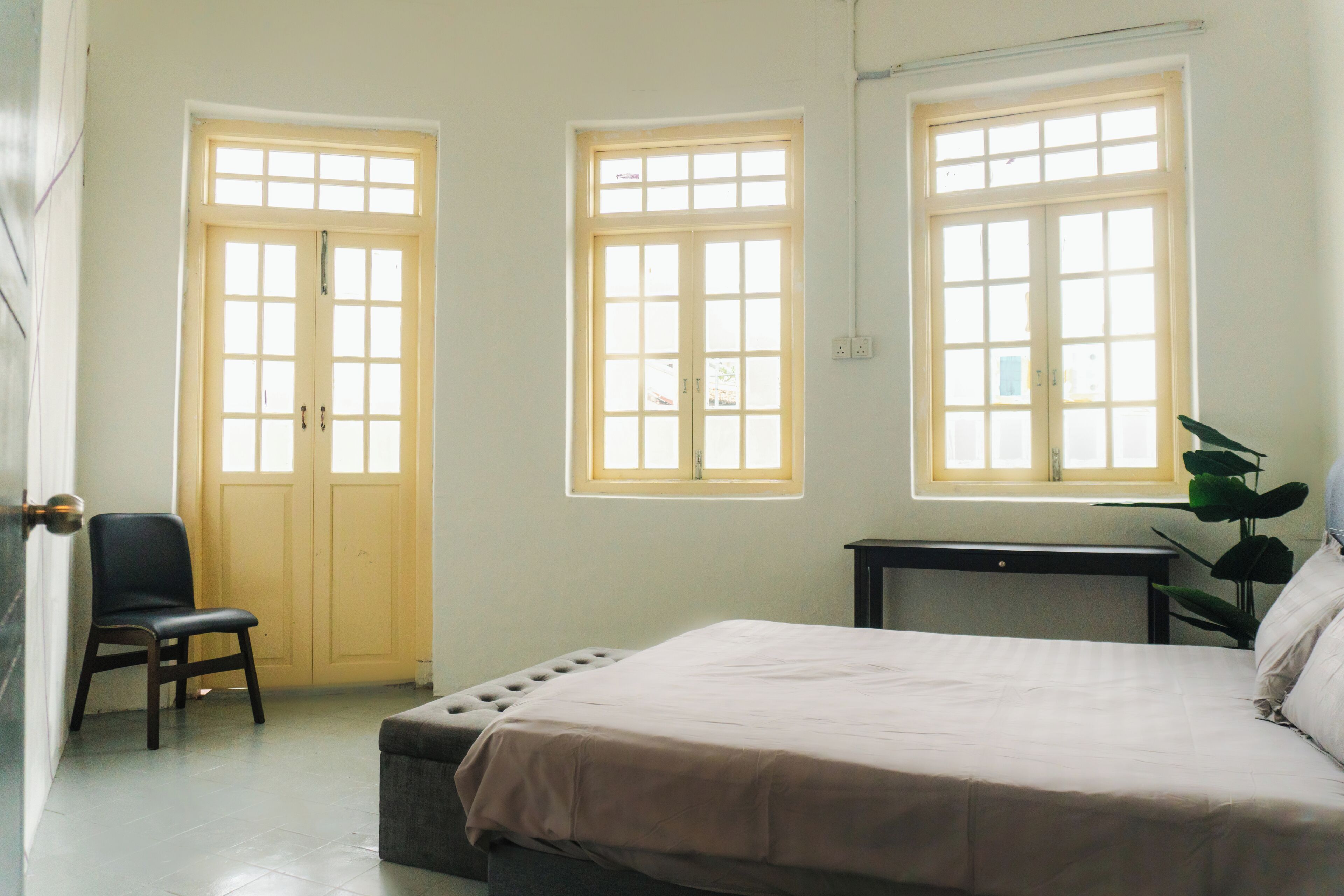 A bedroom with a bed, two windows, a chair, and a small table.