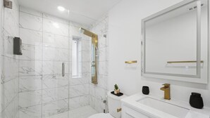 Ein modernes Badezimmer mit einer weißen Marmordusche, einer weißen Toilette, einem weißen Waschbecken und einem großen Spiegel.