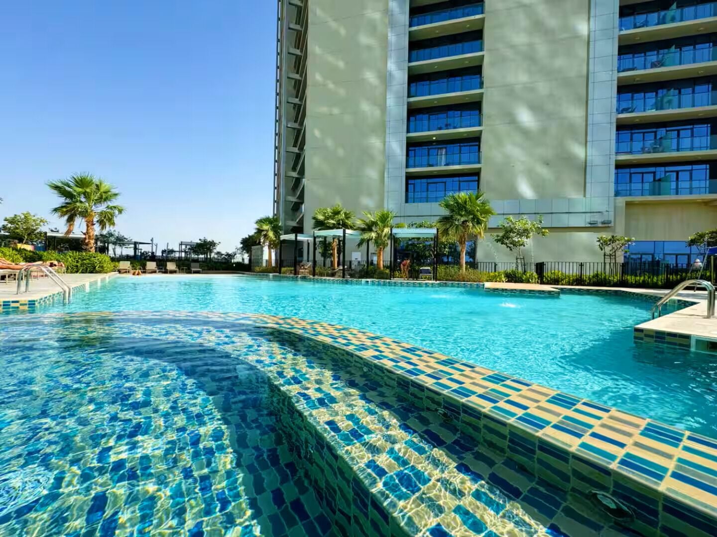 A swimming pool with clear blue water, surrounded by a modern building with multiple floors and balconies.