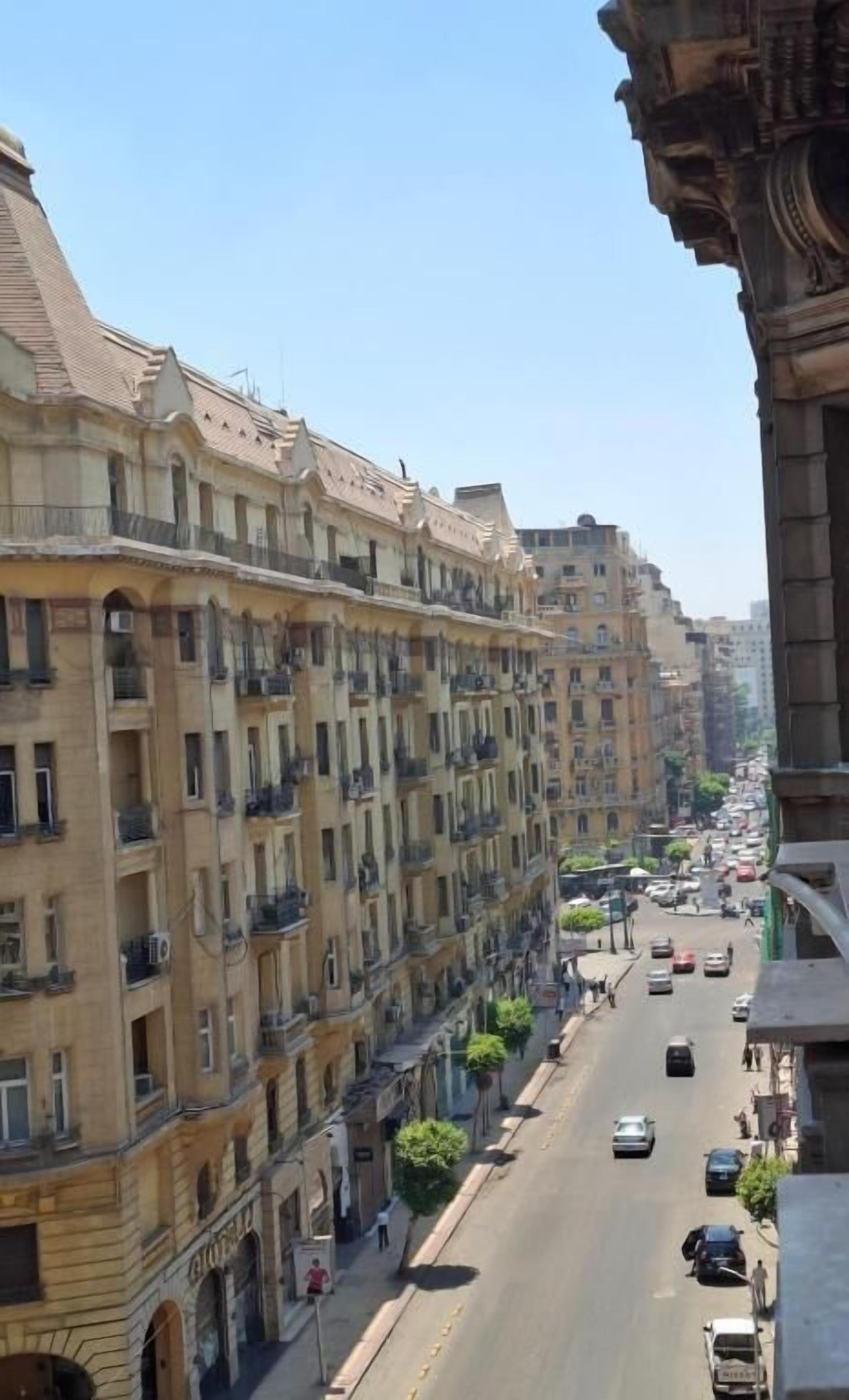 Un edificio de varios pisos con balcones, una calle en su parte delantera y coches aparcados.
