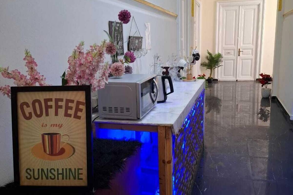 Un área de recepción con estación de café, cartel enmarcado, flores decorativas y suelo pulido.