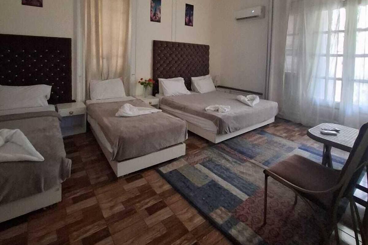 Una habitación de hotel con tres camas, una mesita pequeña y una silla.
