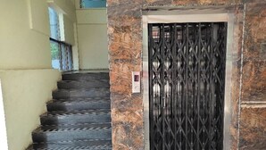 A staircase leading to a door with a metal gate, a marble wall, and a light-colored wall with a window. - SRI SUBHAMASTHU GRAND (Vijayawada)
