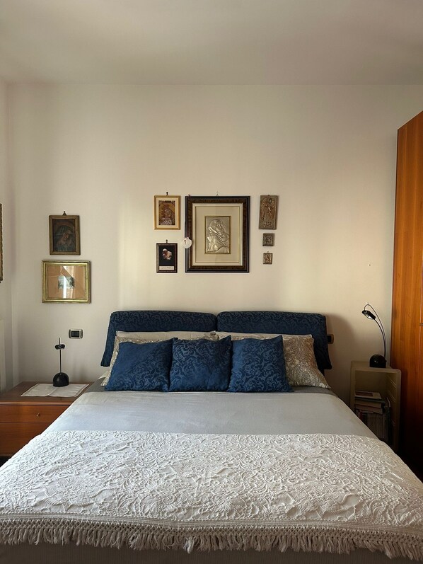 A neatly arranged bedroom with a large bed, a bedside table, a nightstand, and a wall-mounted lamp. - Ketty's House Apartment between sea and mountains (Vico Equense)