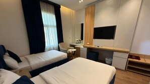 Habitación de hotel moderna con dos camas, un escritorio, una silla, una mesita y un televisor.