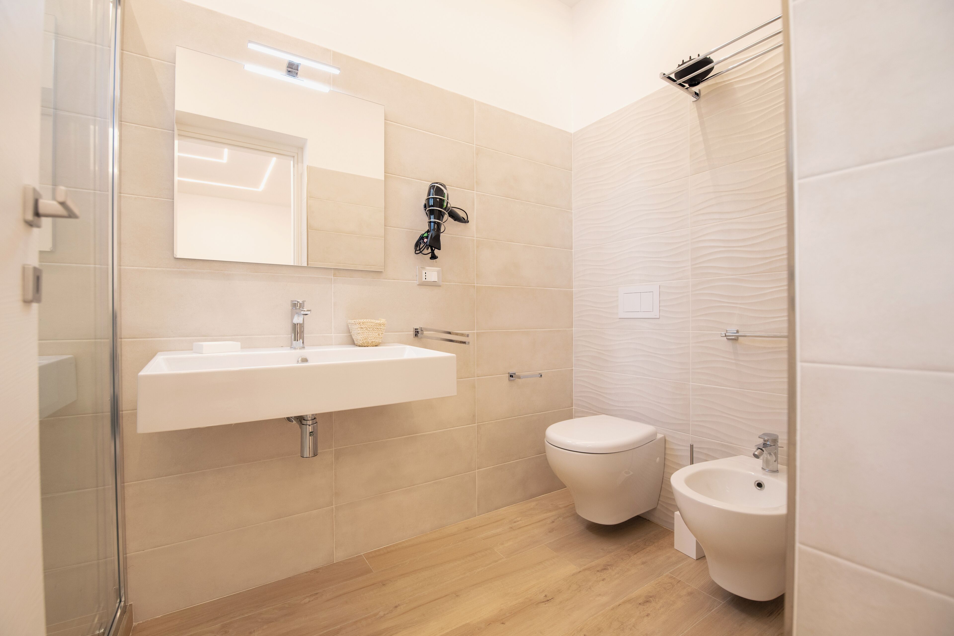 A modern bathroom with a glass shower enclosure, a sink with a mirror, and a bidet.