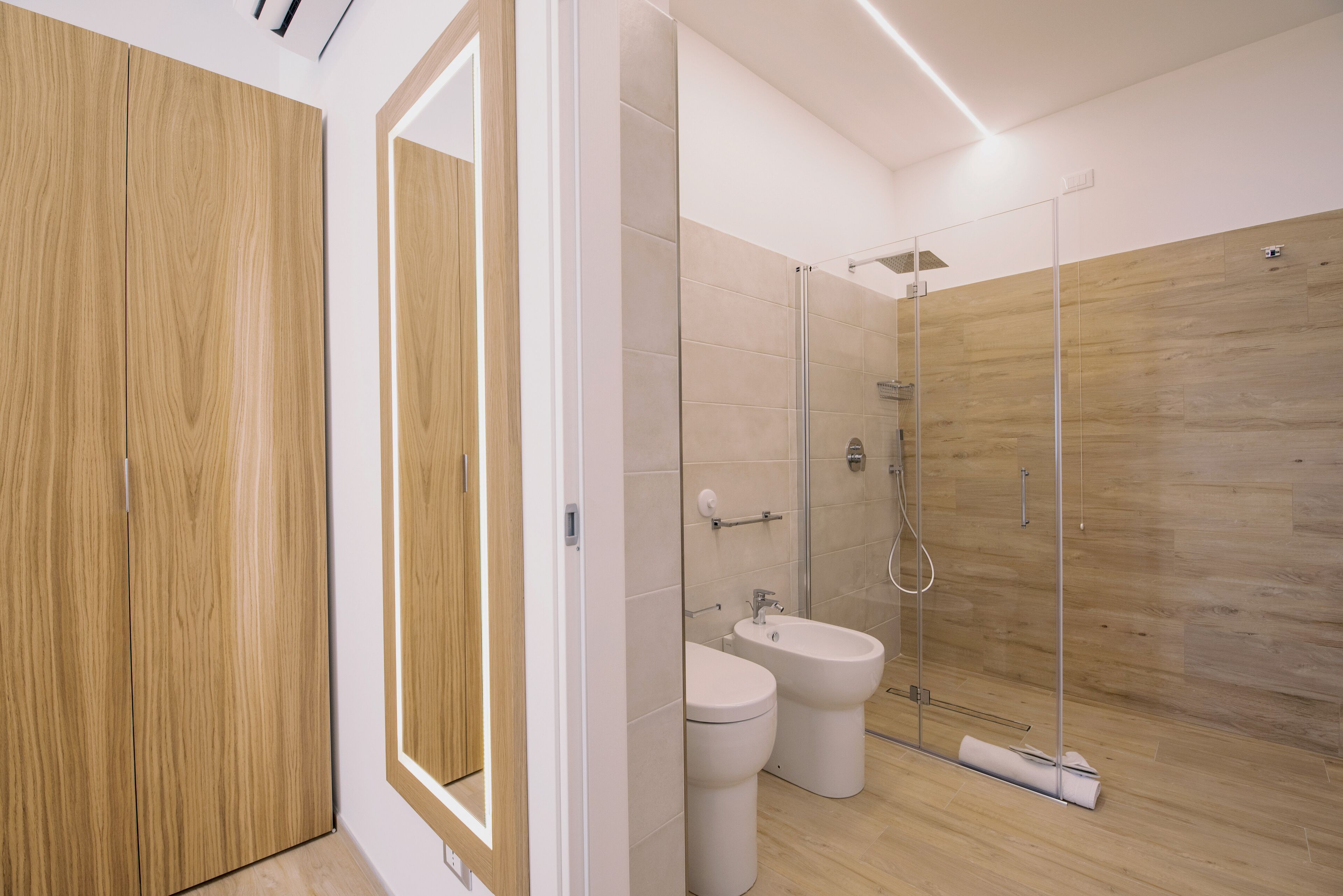Un bagno moderno con pavimento in legno, cabina doccia in vetro, water e bidet.