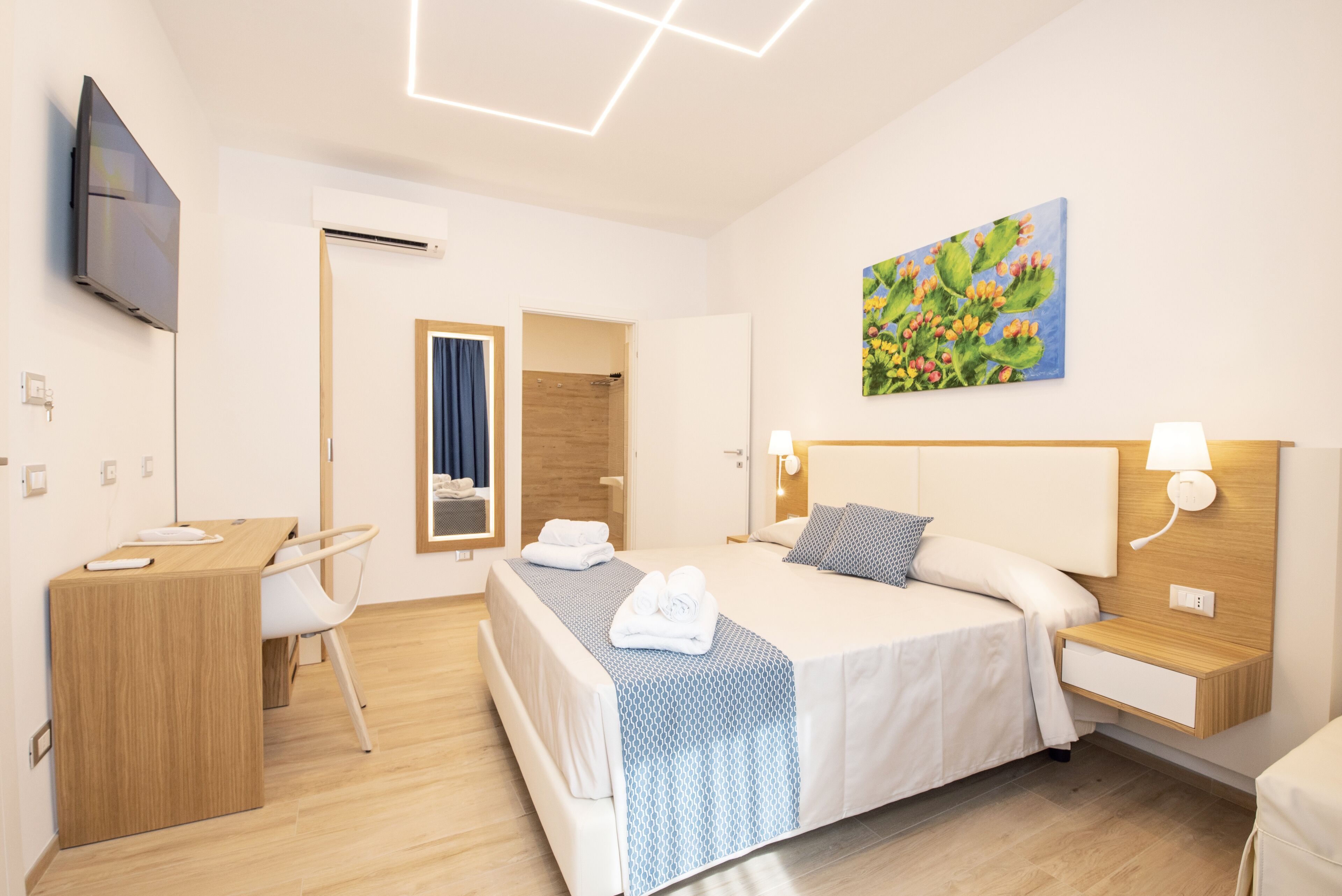 Ein modernes Hotelzimmer mit Bett, Nachttischen, Schreibtisch und Fernseher.