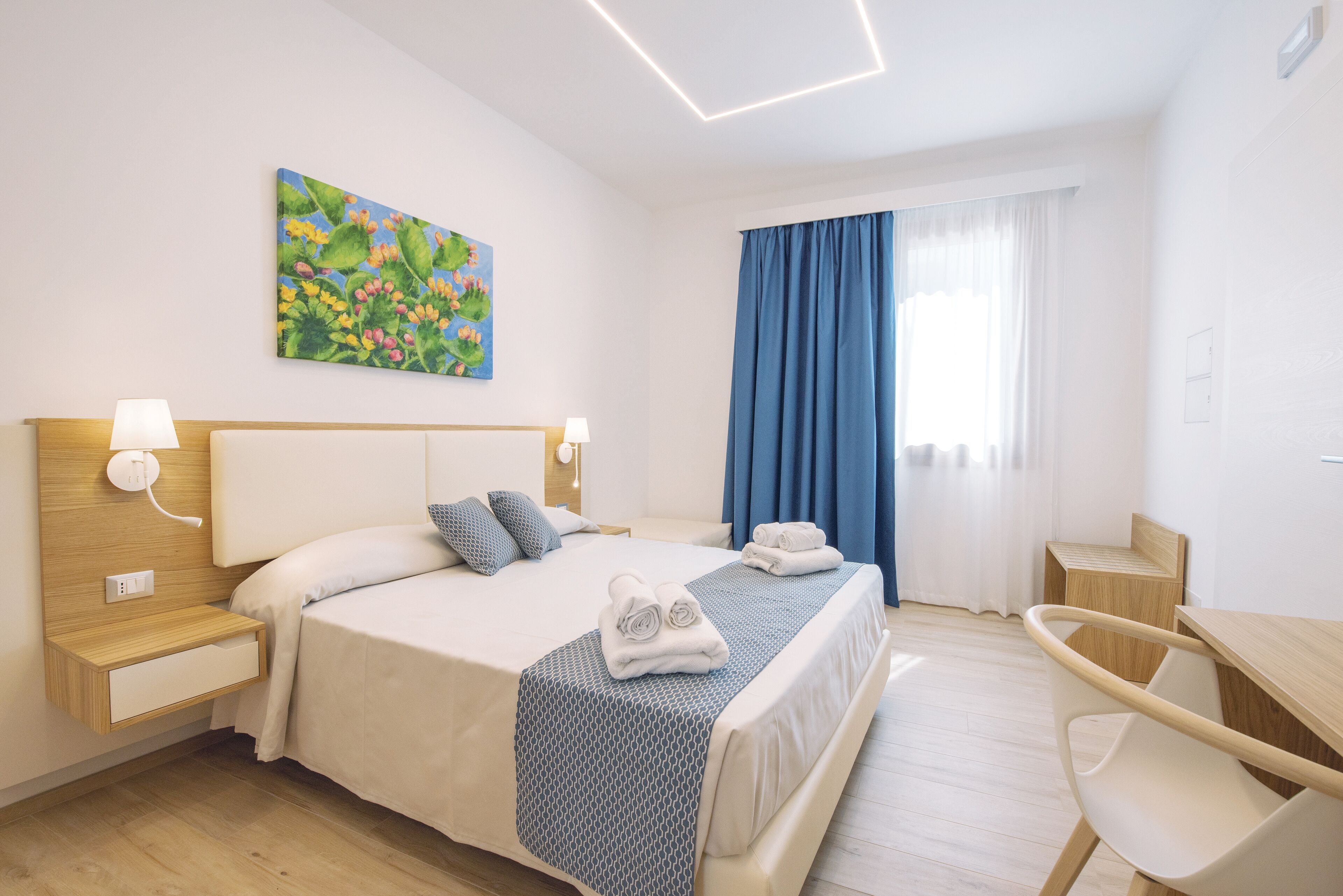A hotel room with a bed, bedside tables, a desk, and a chair.