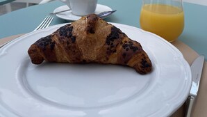 A croissant on a white plate with a glass of orange juice on a table in a cafe setting. - I Mori Hotel  (San Vito Lo Capo)