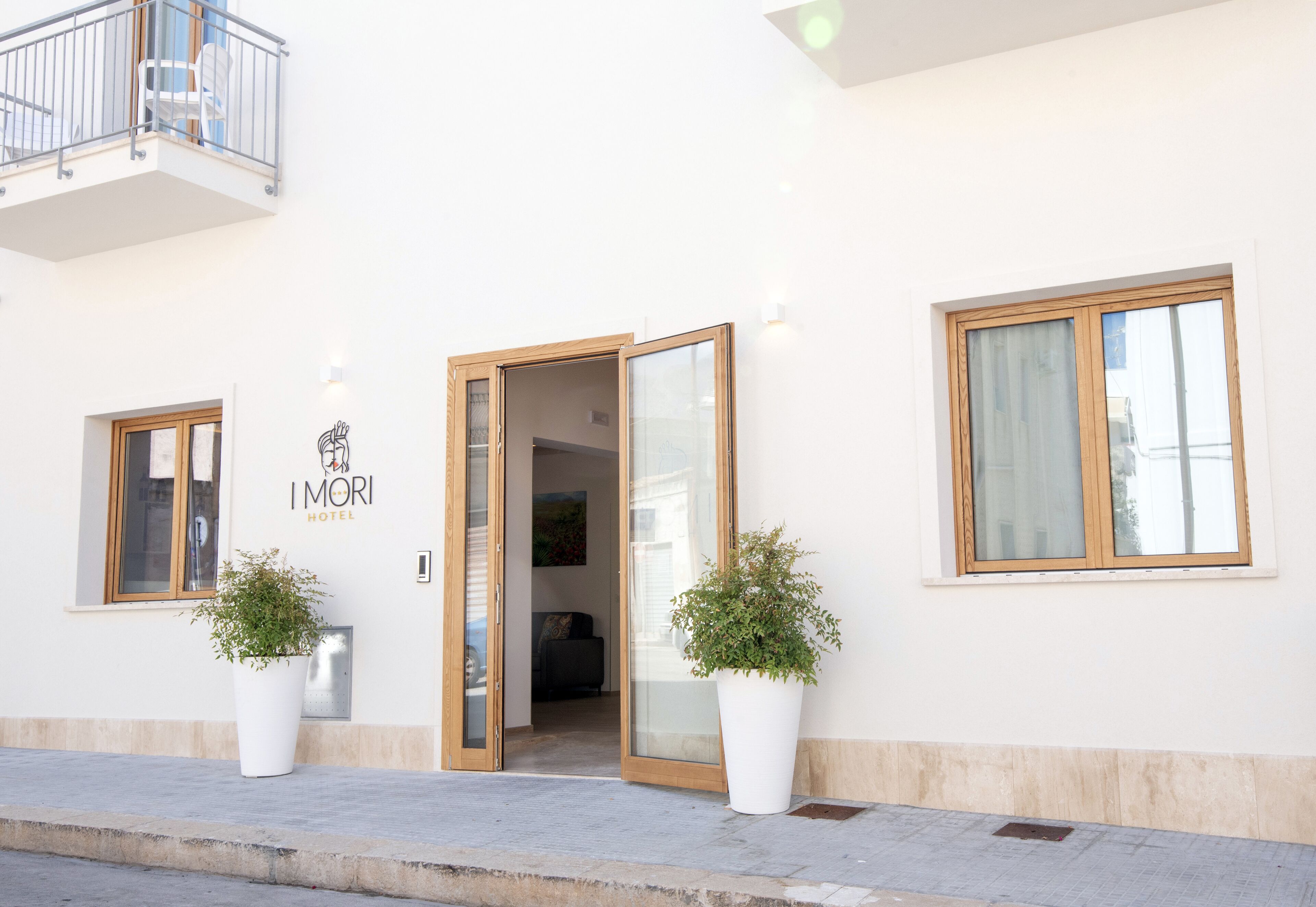 Entrada de un hotel con un letrero que dice 'IMORI HOTEL', dos plantas en macetas y un balcón.