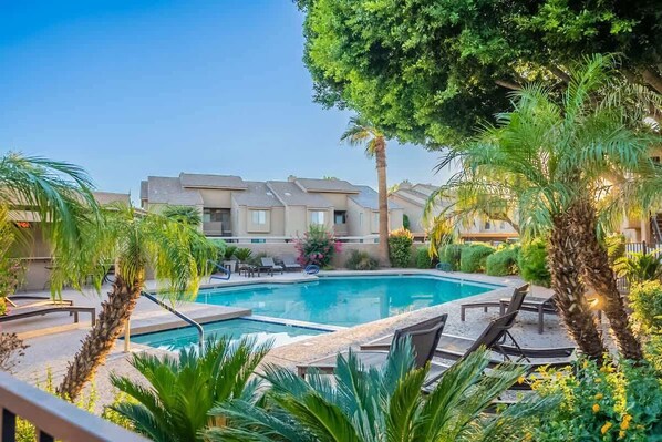 Una piscina rodeada de palmeras y sillas de descanso, con un edificio al fondo.