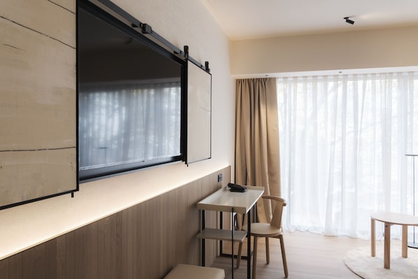 A modern room with a large window, a flat-screen TV mounted on the wall, a small table, and a chair. - Olivia Lisboa Hotel 5* (Lisbon)