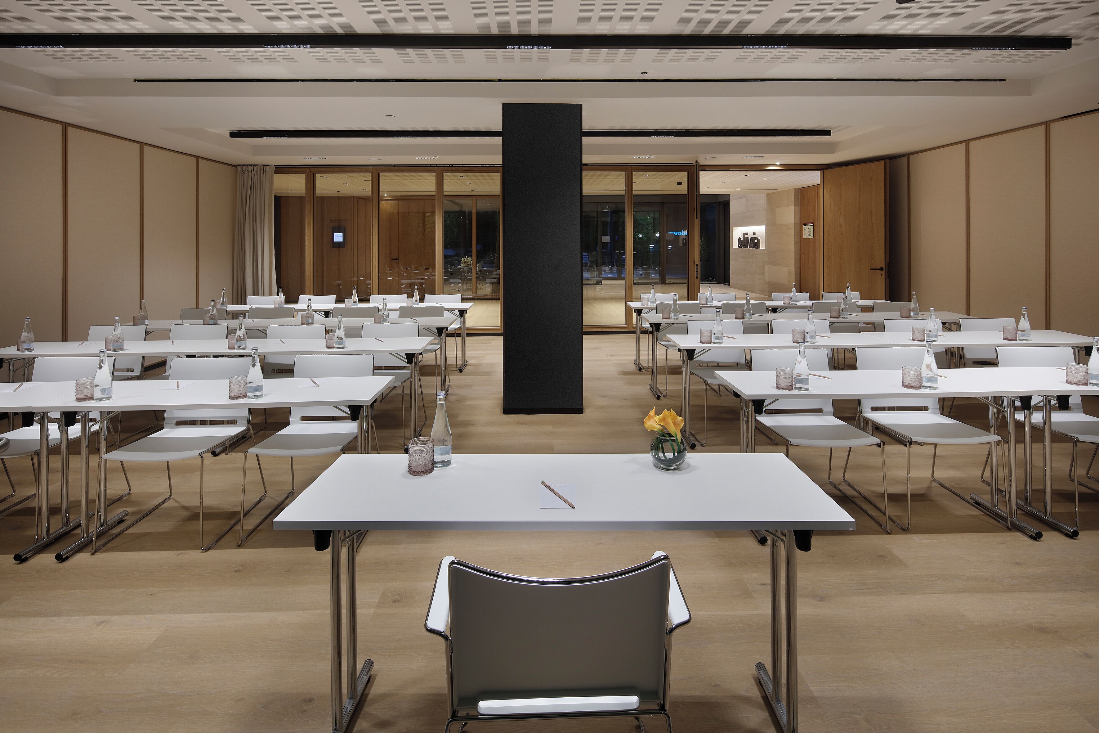 A conference room with tables and chairs, a large pillar, and a view of the lobby.