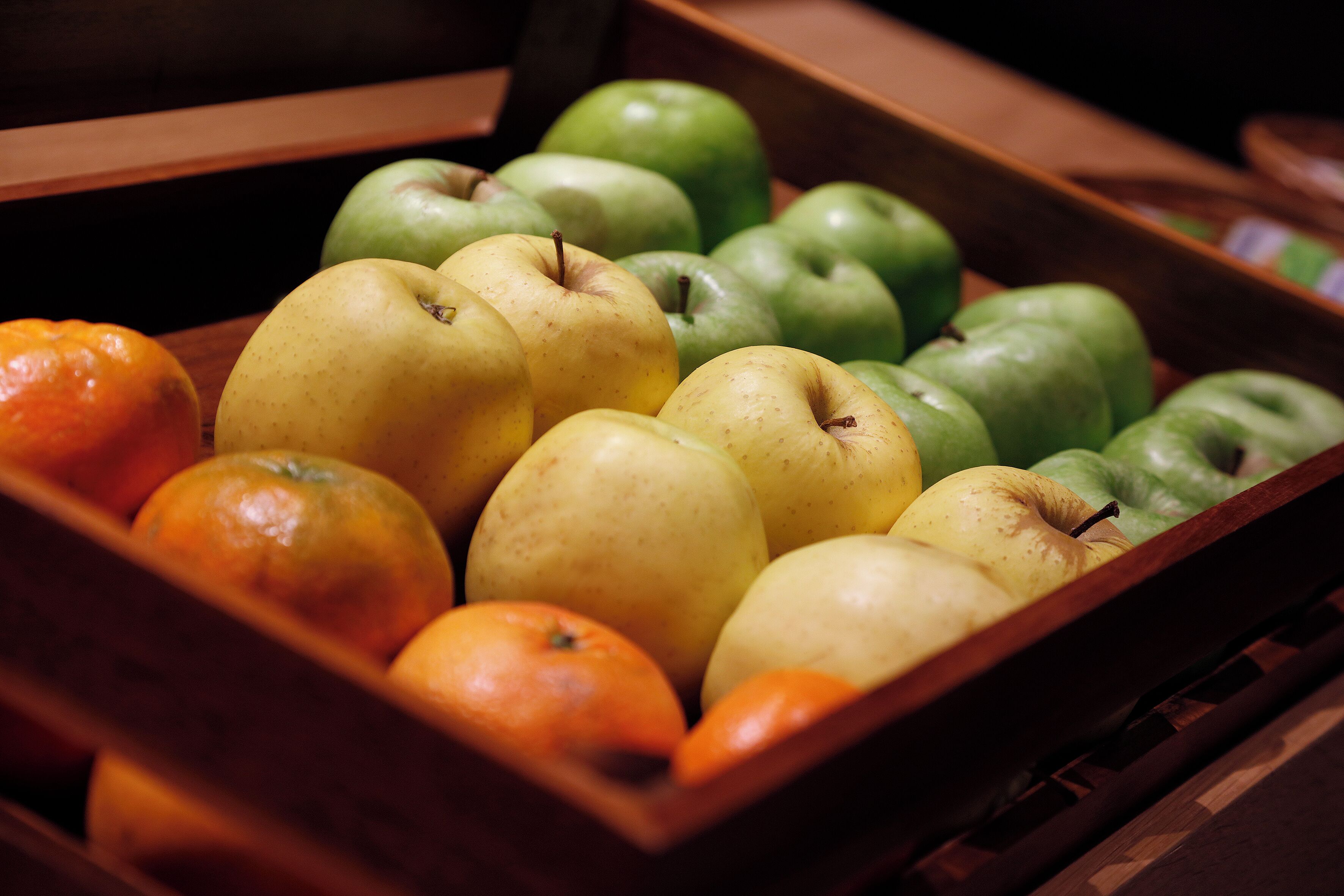 A wooden crate filled with various fruits including apples and oranges.