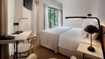 A hotel room with a bed, desk, chair, and a TV mounted on the wall.