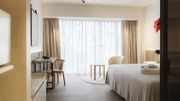 A hotel room with a bed, a desk, a chair, a small round table, and a window with curtains.