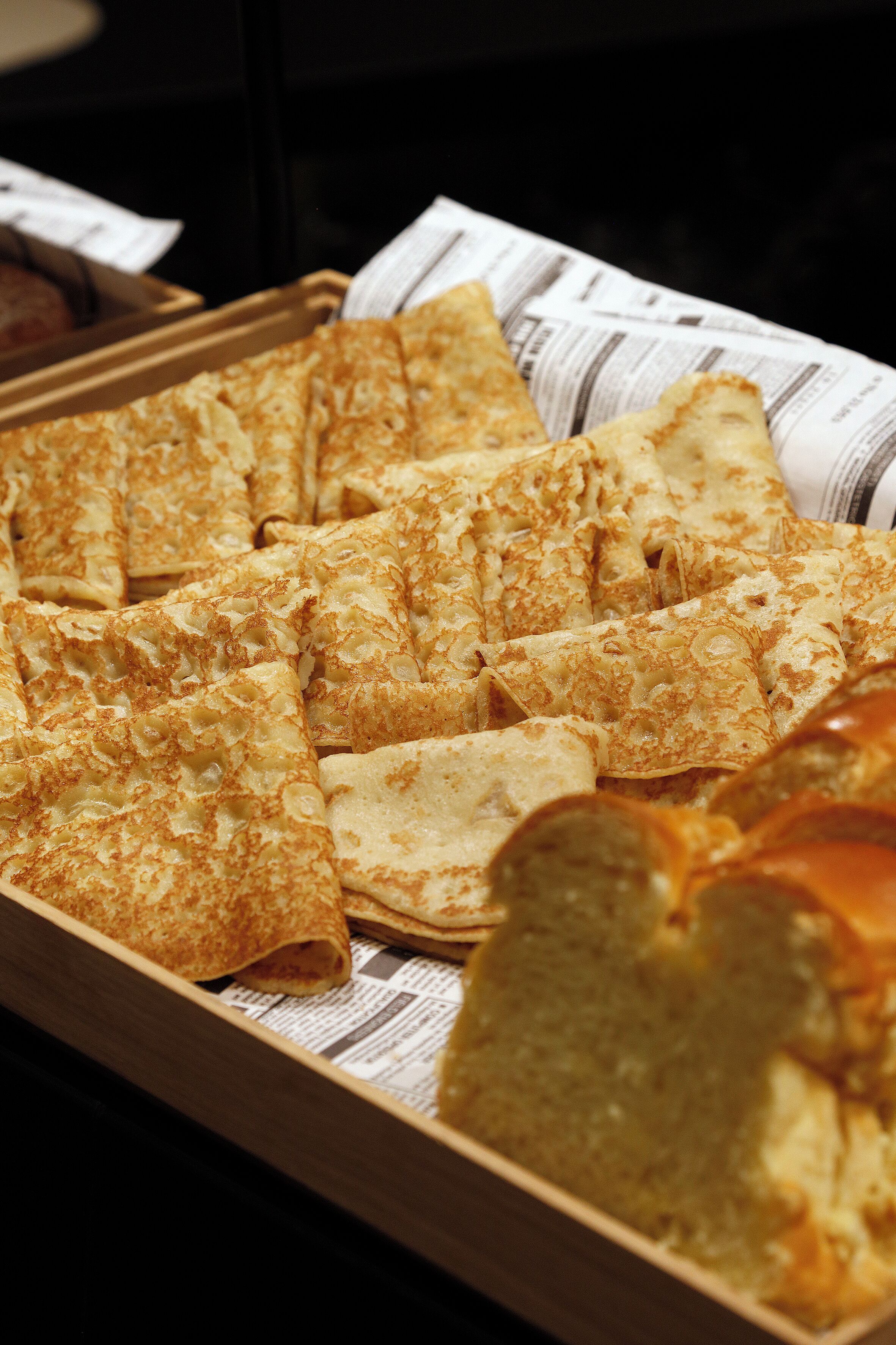 A tray of folded crepes and a loaf of bread on a wooden surface.